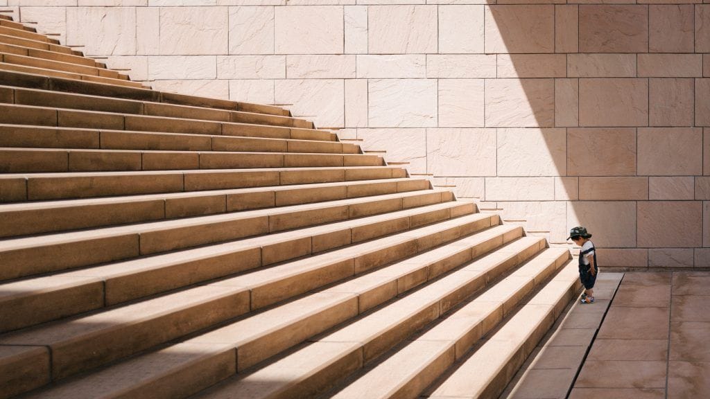 Un niño pequeño frente a una escalera, representando los pasos que hay que dar, para llegar a un lugar distinto.
